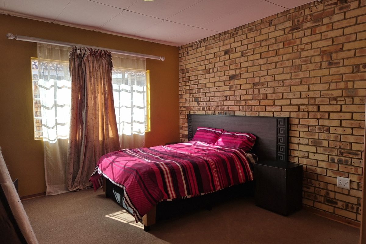 A bedroom featuring an exposed brick accent wall, carpeted flooring, and natural light from the window.