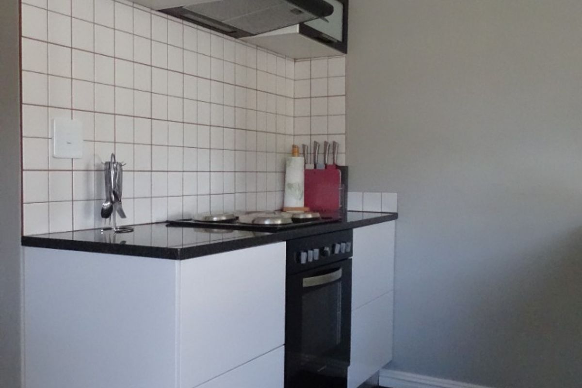 Compact kitchen featuring modern white cabinetry, black countertops, a built-in oven, and a tiled backsplash.