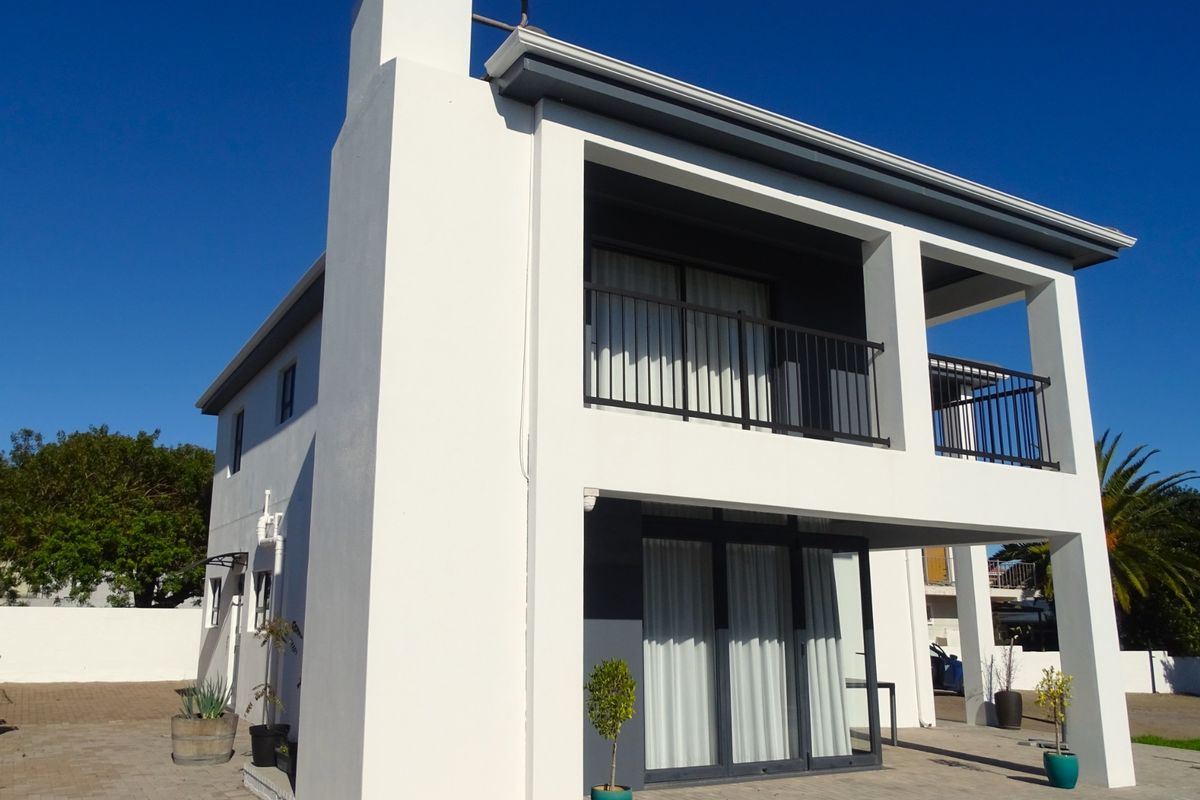 Rear view of a modern two-story house featuring a covered patio, upper-level balcony with metal railings, and a swimming pool area.