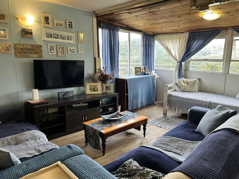 A cozy living room featuring large windows with natural light, timber-clad ceiling, and wood-look flooring, offering a comfortable and relaxed atmosphere.