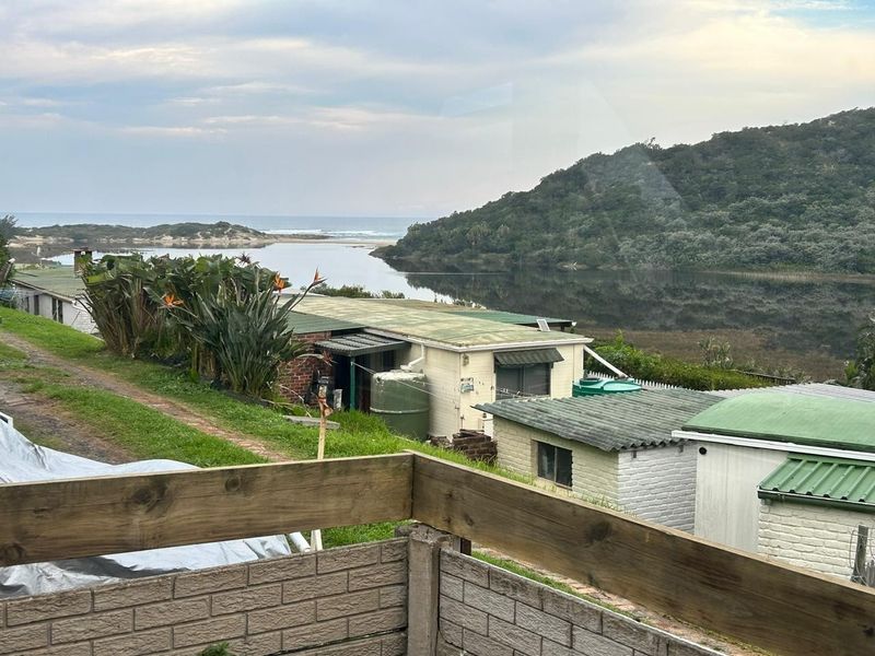 Elevated view overlooking a coastal lagoon and surrounding landscape, featuring multiple small residential structures with corrugated roofing and brickwork.