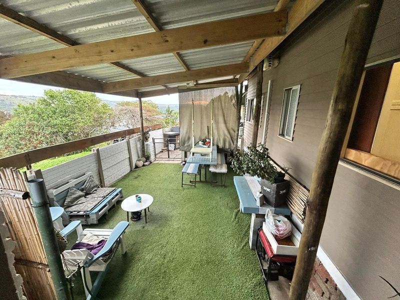 A covered outdoor patio area featuring artificial turf, timber structural beams, and a corrugated metal roof, providing a functional space for outdoor relaxation.