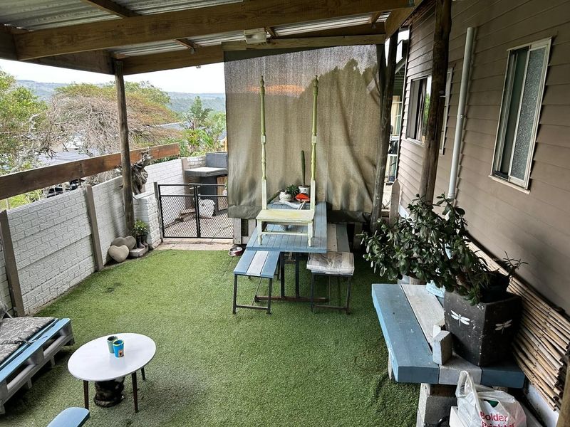 Covered outdoor patio area featuring artificial turf, timber roof structure, and a built-in brick wall, offering a functional space for outdoor relaxation.