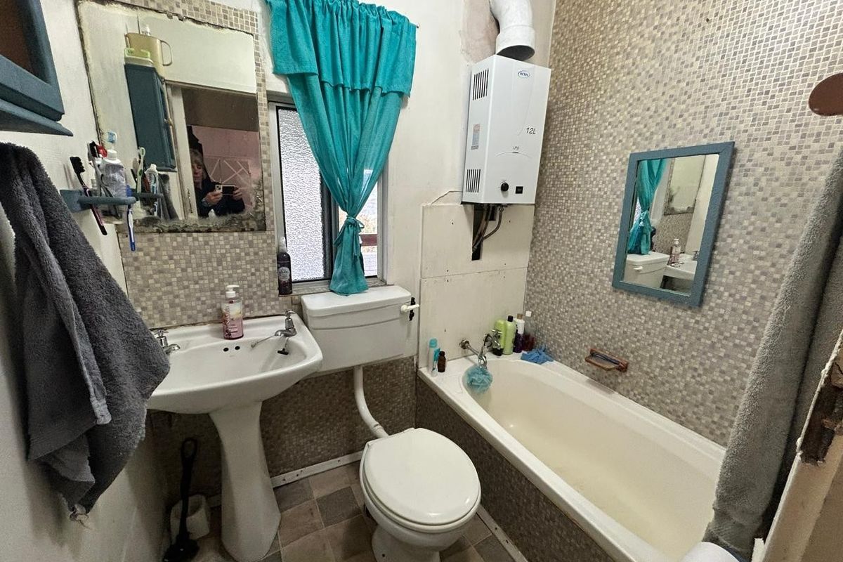 Compact bathroom featuring a pedestal basin, toilet, and bathtub with wall-mounted gas geyser, requiring significant renovation and modernization of finishes.