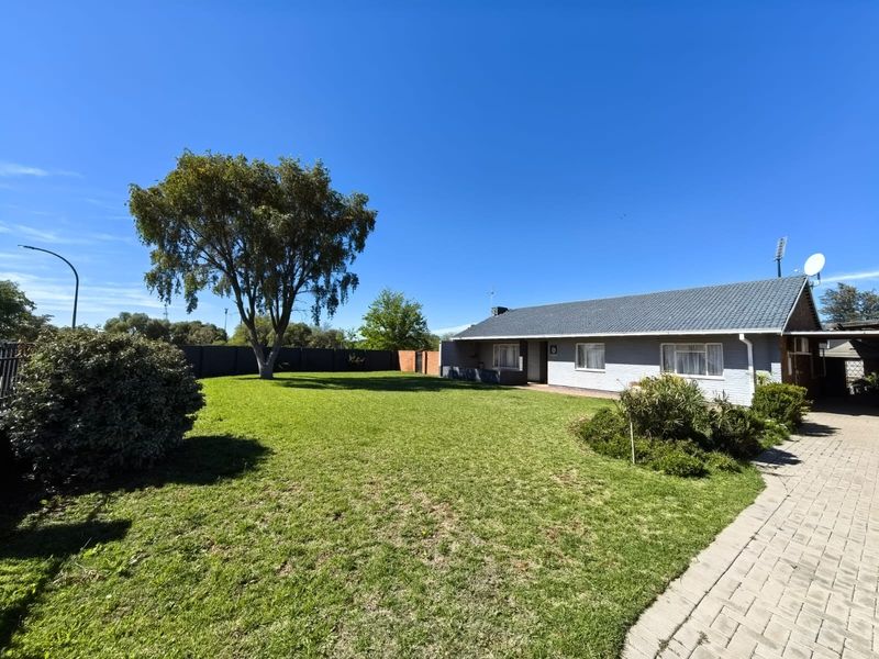 Spacious rear garden featuring a well-maintained lawn, paved driveway, and a single-story house with a tiled roof.