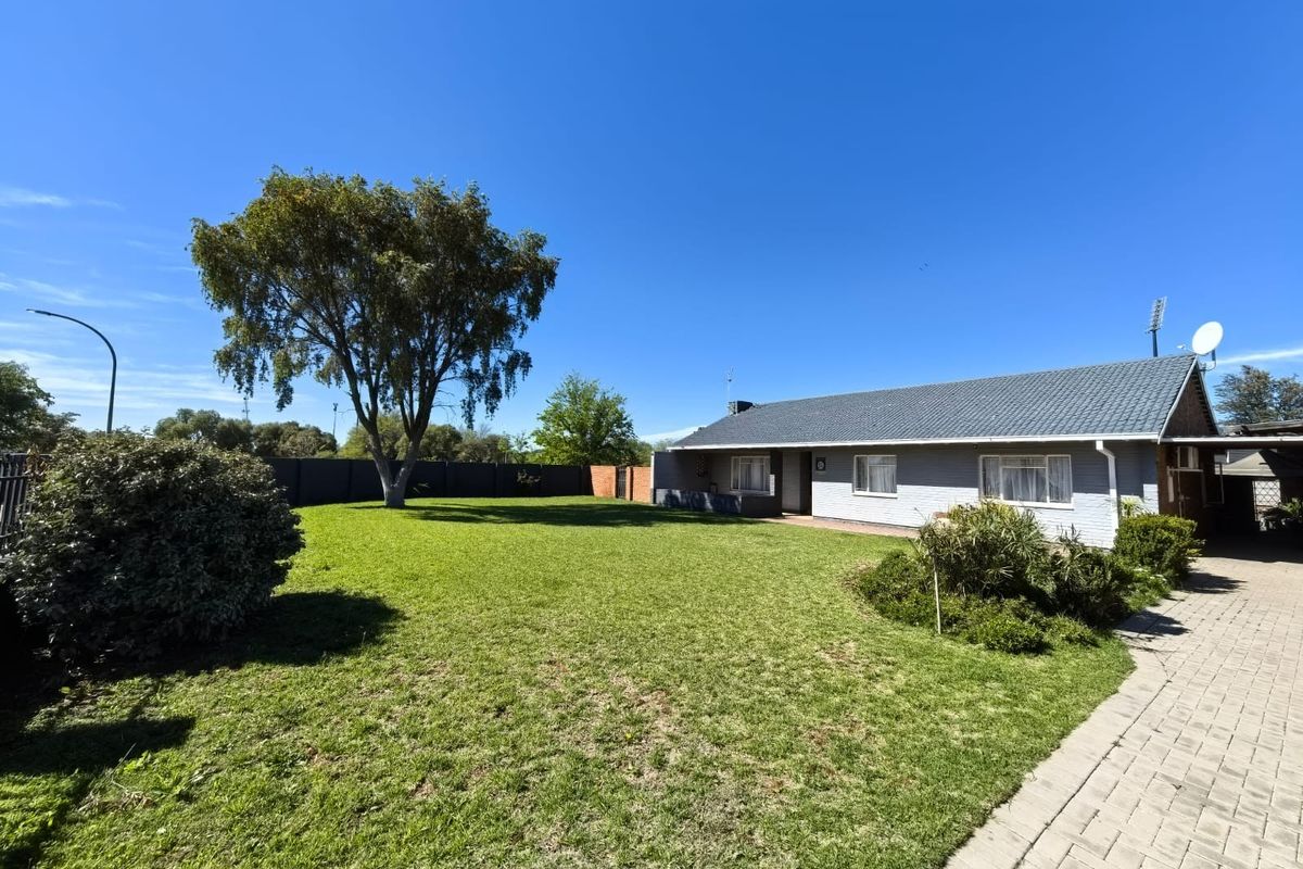 Spacious rear garden featuring a well-maintained lawn, paved driveway, and a single-story house with a tiled roof.