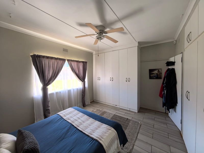 A bedroom featuring tiled flooring, a ceiling fan, and extensive built-in cupboard storage.