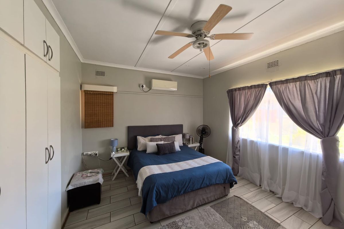 A well-maintained bedroom featuring built-in cupboards, a ceiling fan, split-system air conditioning, and modern tiled flooring.