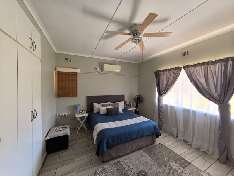 A well-maintained bedroom featuring built-in cupboards, a ceiling fan, split-system air conditioning, and modern tiled flooring.