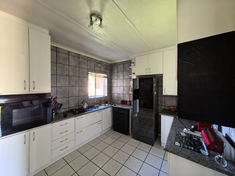A functional kitchen featuring white cabinetry, granite countertops, a built-in oven, gas hob, and grey tiled splashbacks with tiled flooring.