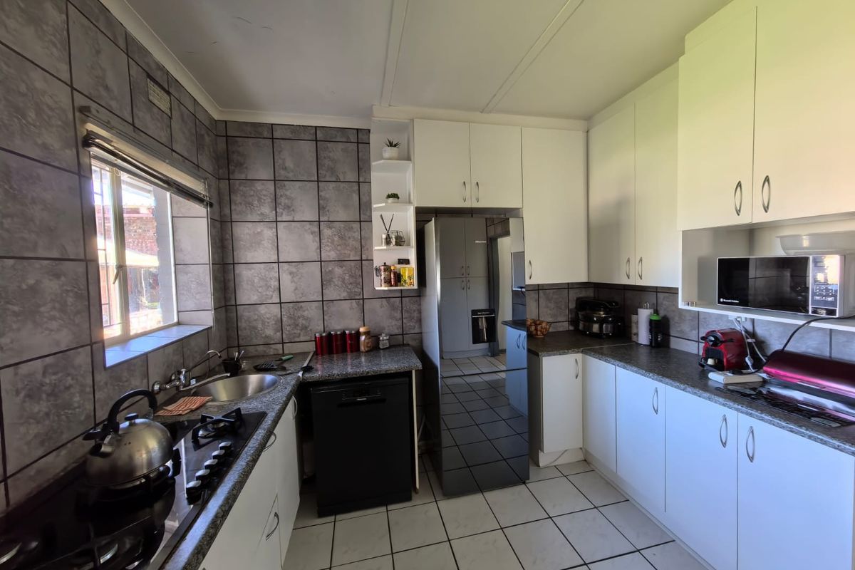 Functional kitchen featuring granite countertops, gas hob, built-in oven, integrated dishwasher, and ample white cabinetry with grey tiled splashbacks.