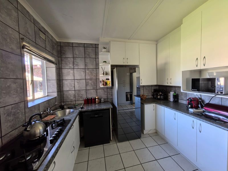 Functional kitchen featuring granite countertops, gas hob, built-in oven, integrated dishwasher, and ample white cabinetry with grey tiled splashbacks.
