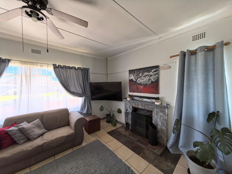 A living room featuring a brick fireplace, tiled flooring, and a ceiling fan, offering a comfortable and functional space.