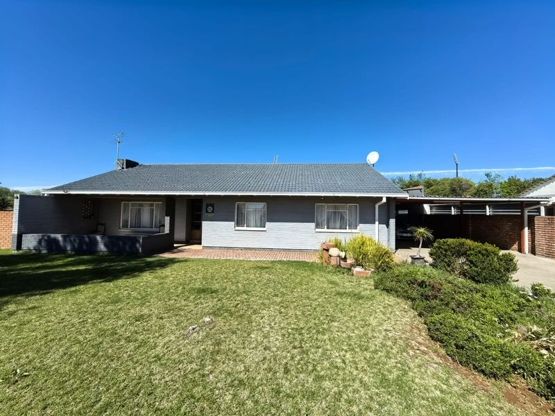 Front elevation of a single-story brick house featuring a tiled roof, attached carport, and a well-maintained front lawn.