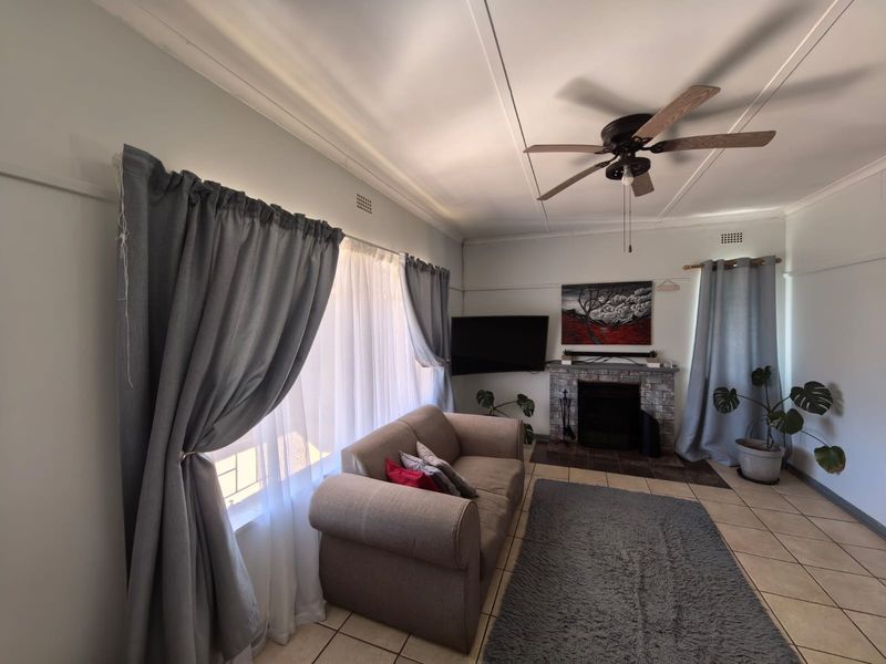 A living room featuring tiled flooring, a brick fireplace, and a ceiling fan, offering a comfortable and functional space.