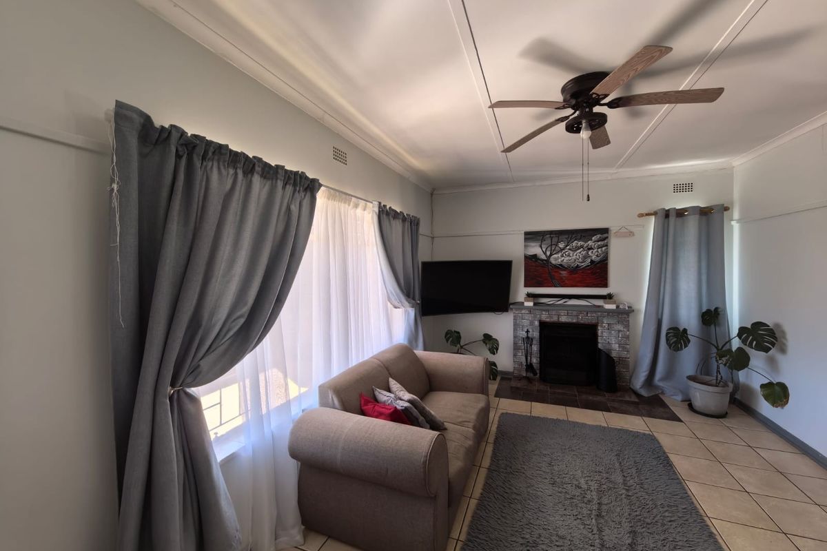 A living room featuring tiled flooring, a brick fireplace, and a ceiling fan, offering a comfortable and functional space.