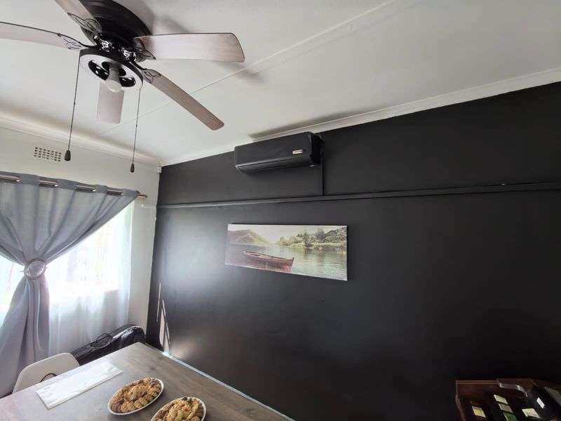 A living area featuring a dark accent wall, a ceiling fan, and a wall-mounted split-system air conditioner.