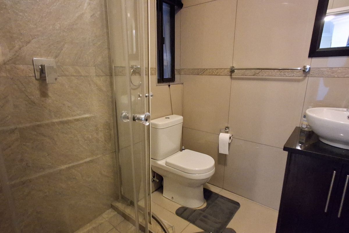 A compact, modern bathroom featuring a glass-enclosed shower, a white ceramic toilet, and a vessel sink mounted on a dark vanity cabinet.