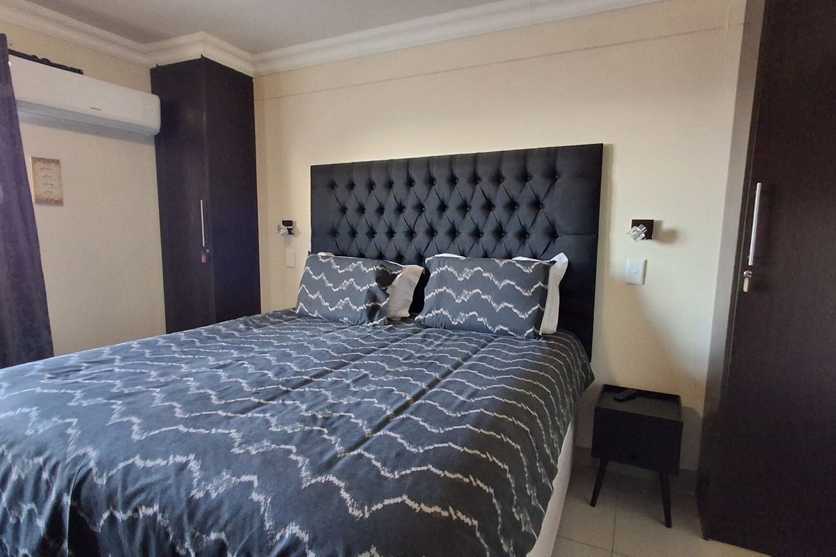A well-maintained bedroom featuring built-in dark wood cabinetry, a wall-mounted air conditioning unit, and crown molding.
