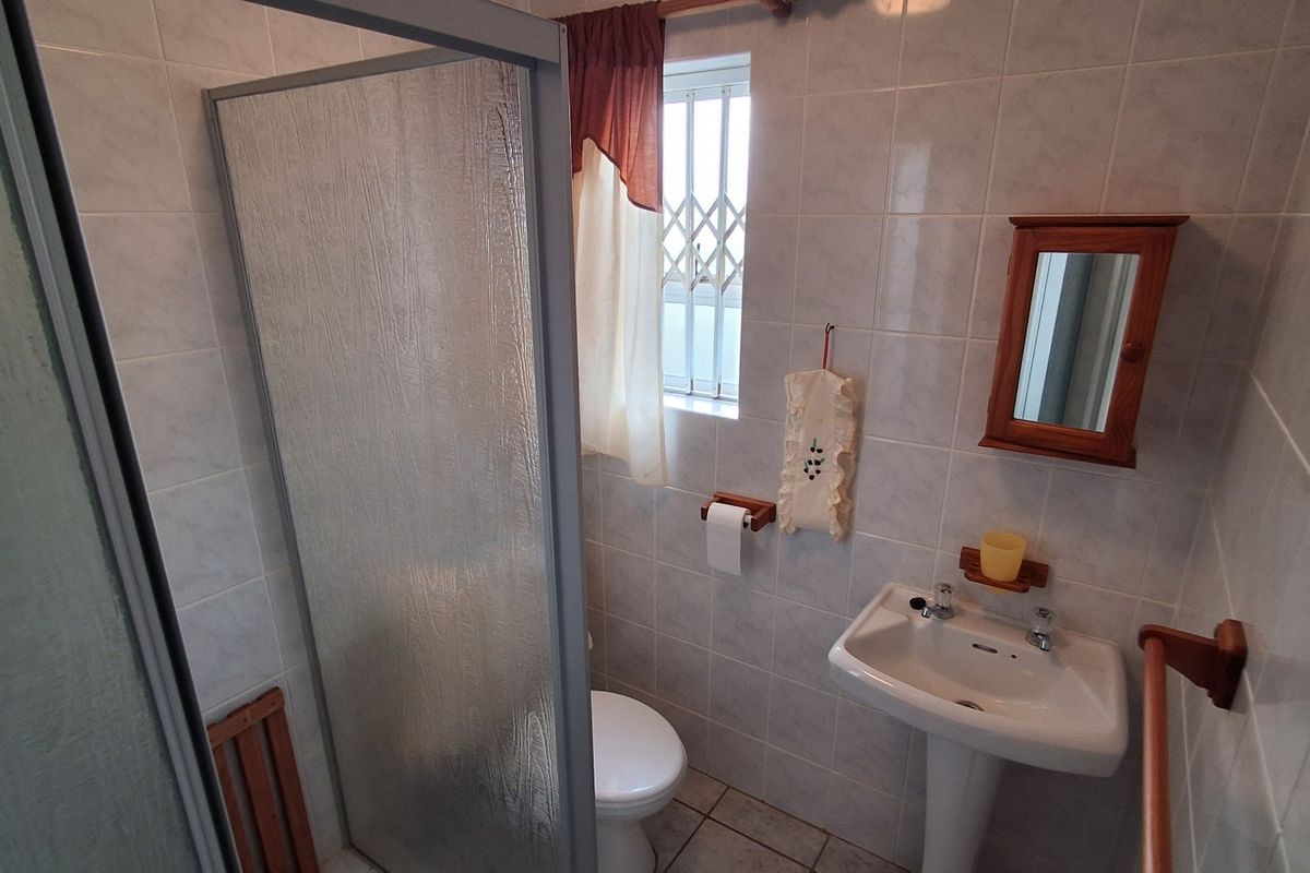A compact bathroom featuring a shower enclosure, pedestal basin, and toilet with tiled walls and a security-grille window.