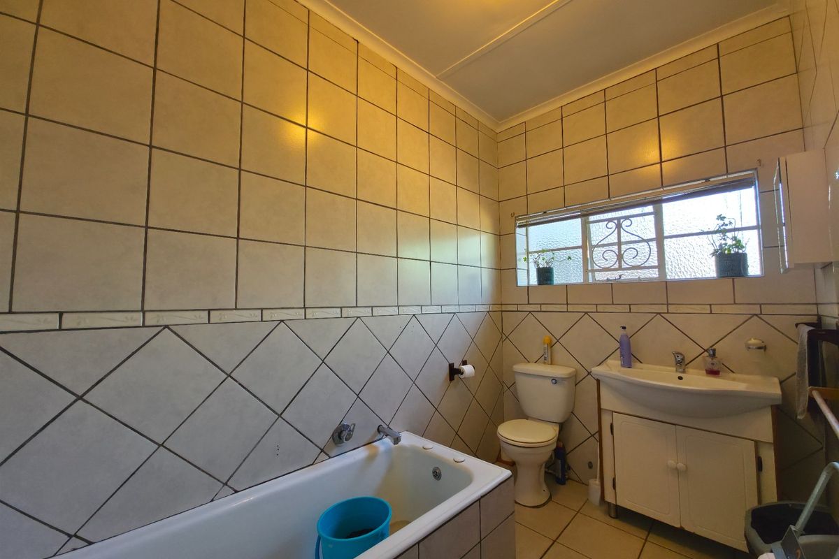 A functional bathroom featuring a bathtub, toilet, and vanity basin with tiled walls and flooring, offering a dated but practical layout.