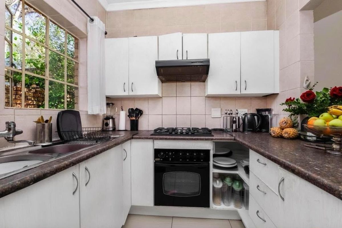 A functional kitchen featuring white cabinetry, dark laminate countertops, a gas hob, built-in oven, and a tiled splashback with a window view.
