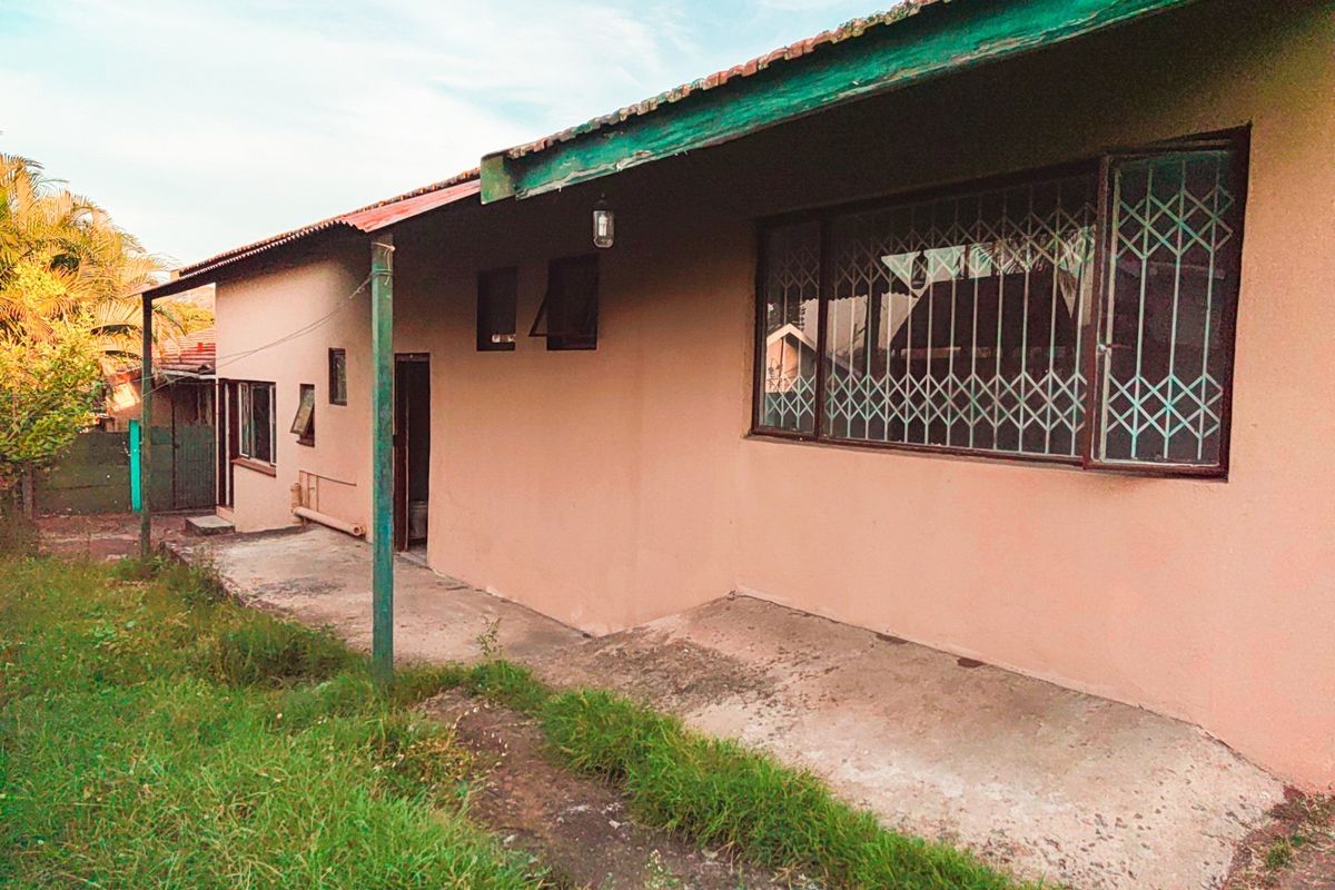Rear exterior view of the house featuring a concrete patio area, security gates on windows, and a corrugated metal roof with weathered timber fascia.