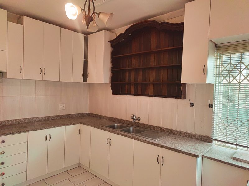 A functional kitchen featuring white cabinetry, granite-look countertops, a double stainless steel sink, and a decorative wooden wall-mounted shelving unit.