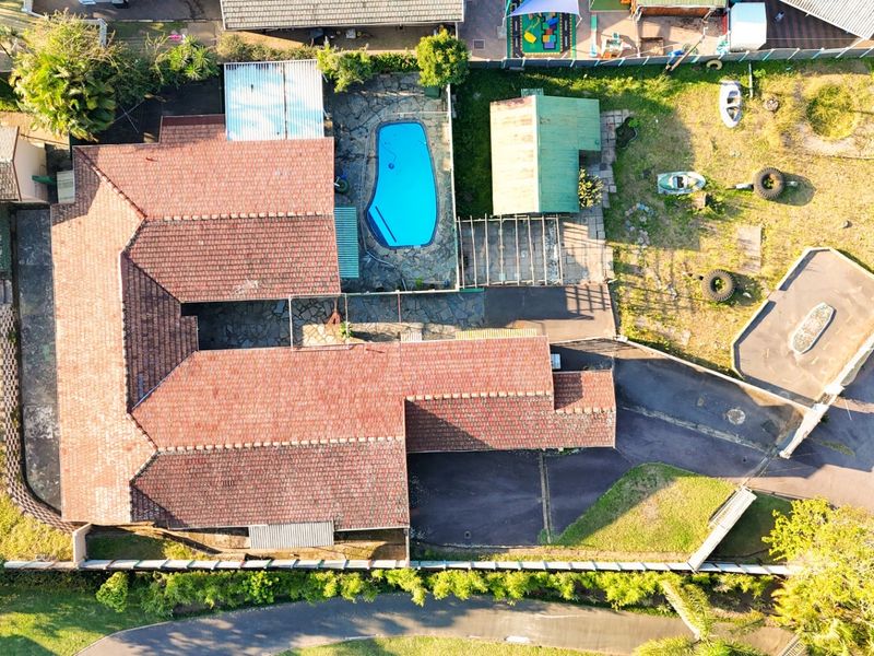 Aerial view of the property featuring a tiled roof, swimming pool, paved patio area, and surrounding garden space.