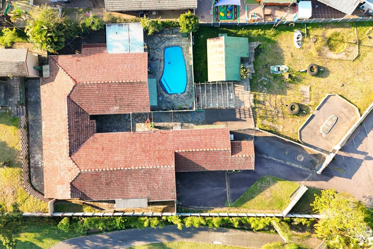 Aerial view of the property featuring a tiled roof, swimming pool, paved patio area, and surrounding garden space.