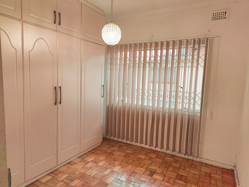 A bedroom featuring built-in floor-to-ceiling cabinetry, parquet wood flooring, and vertical window blinds with security gate.