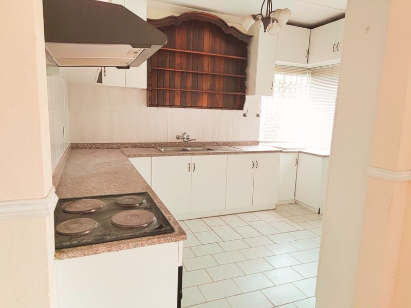 A functional kitchen featuring white cabinetry, a built-in electric hob, extractor fan, and tiled flooring with ample counter space.