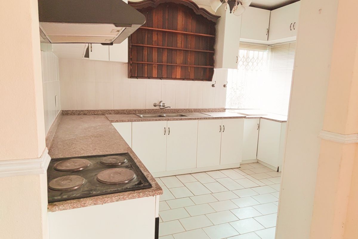 A functional kitchen featuring white cabinetry, a built-in electric hob, extractor fan, and tiled flooring with ample counter space.