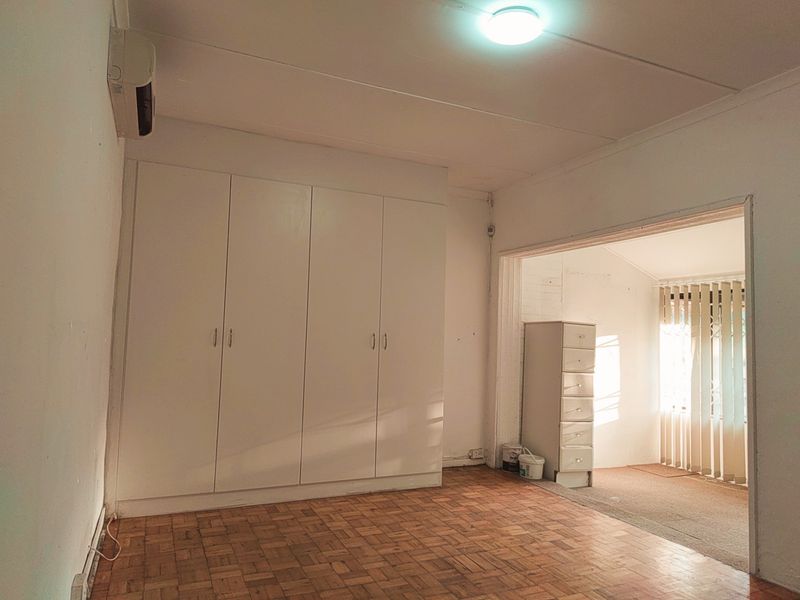 A bedroom featuring built-in wardrobes, parquet flooring, and an integrated air conditioning unit, leading into an adjacent sunroom area.