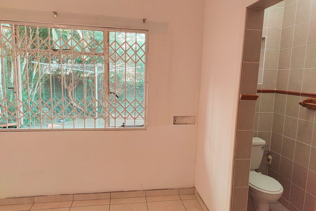 A view of an interior space featuring tiled flooring, a window with security bars, and an adjacent bathroom with tiled walls and a toilet.