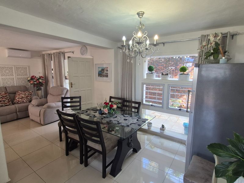 Open plan dining and living area featuring tiled flooring, a decorative chandelier, and large windows with security bars.