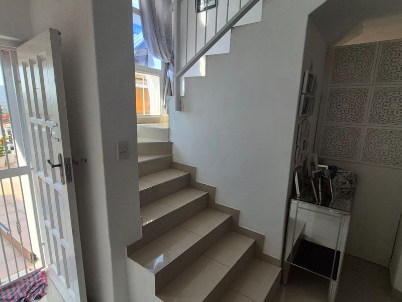 Interior entrance area featuring a tiled staircase with metal balustrades and a security gate leading to an outdoor patio space.