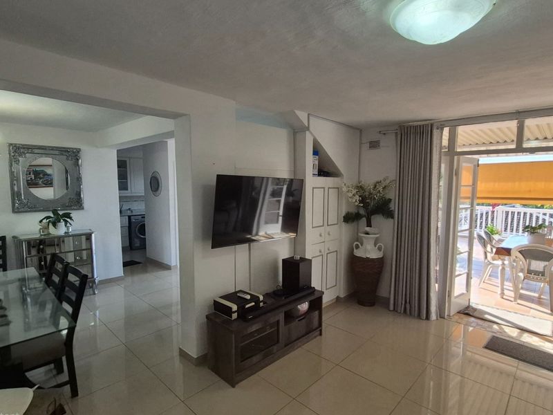 Open-plan living and dining area featuring tiled flooring, built-in storage, and direct access to a covered patio through glass doors.