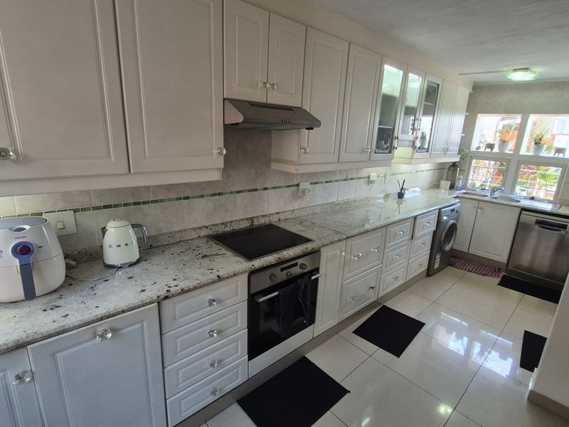 A functional kitchen featuring white cabinetry, granite countertops, a built-in oven, hob, extractor fan, and integrated space for laundry appliances.