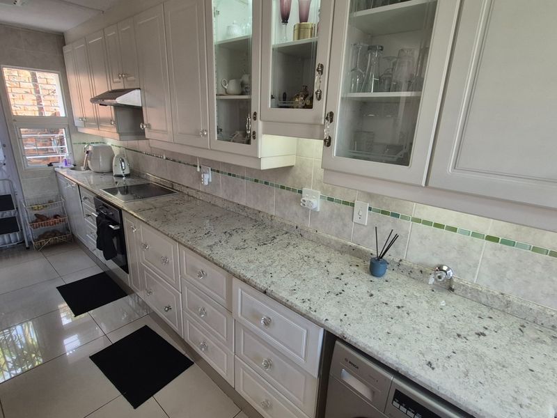 A well-maintained kitchen featuring granite countertops, white cabinetry with glass-front display units, tiled backsplash, and integrated oven and extractor fan.