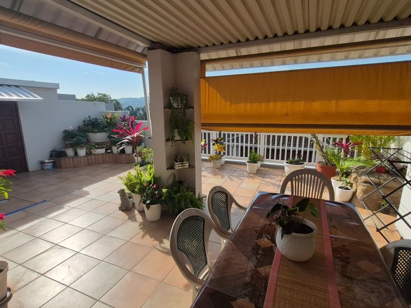 A covered outdoor patio area featuring tiled flooring, a corrugated roof, and a retractable privacy screen, offering a functional space for outdoor living.