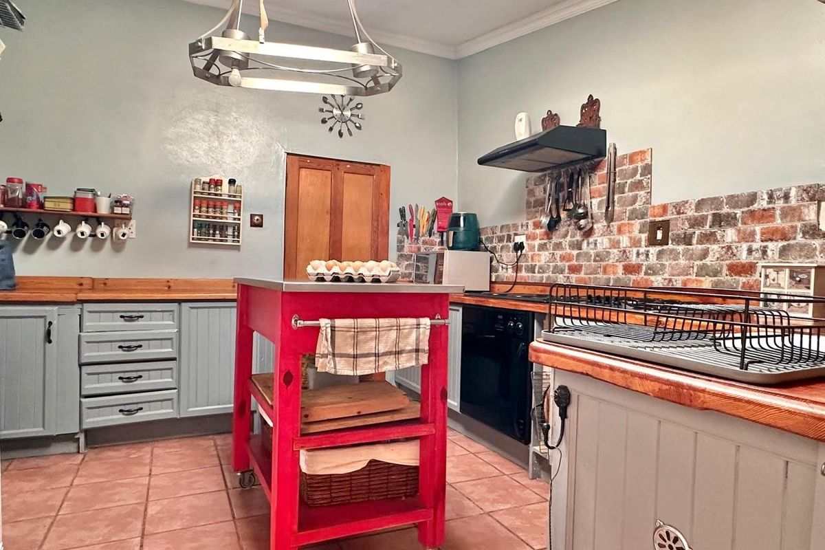 A rustic-style kitchen featuring exposed brick backsplash, wooden countertops, shaker-style cabinetry, and a central mobile island unit.