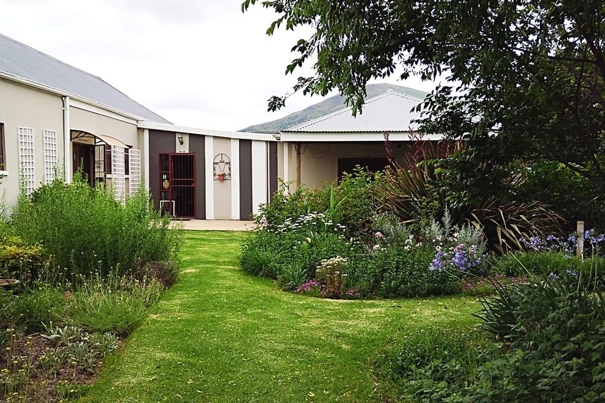 A well-maintained rear garden area featuring a lush lawn, established flower beds, and a covered patio space attached to the building structure.
