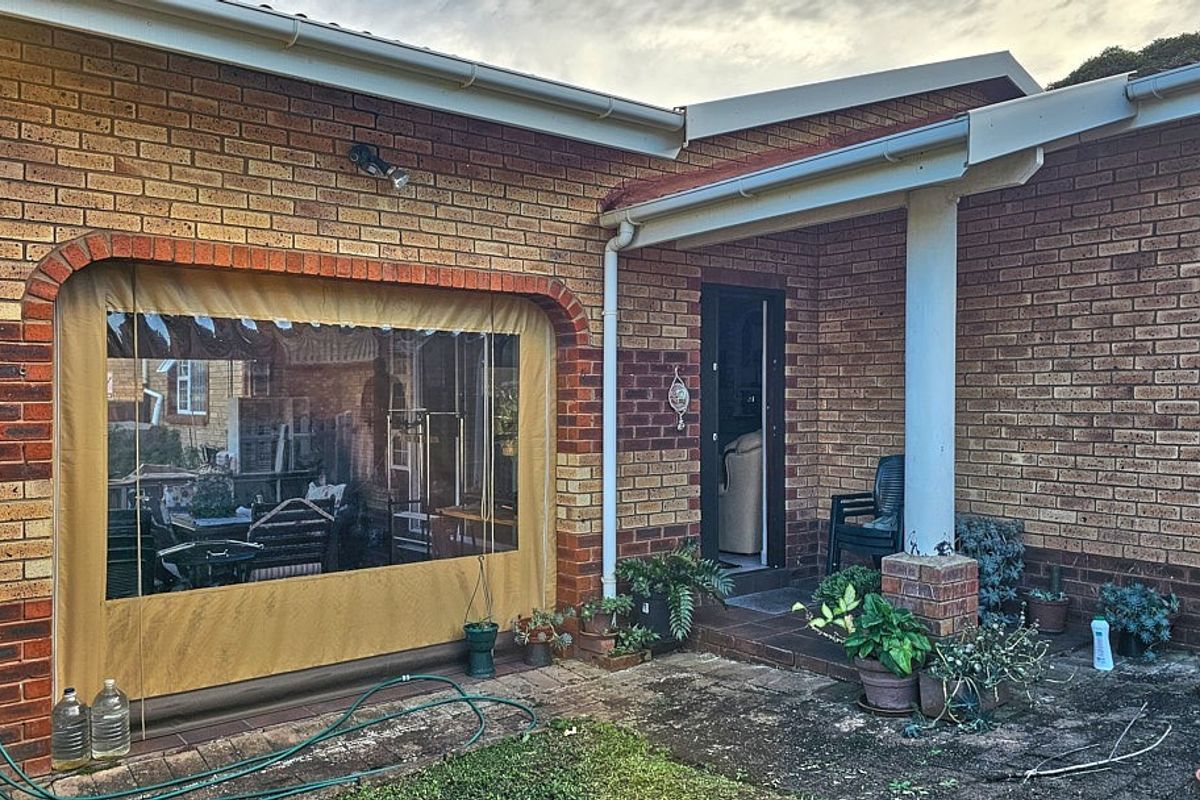 A rear patio area featuring face-brick walls, a covered section with a protective screen, and paved flooring leading to the main entrance.