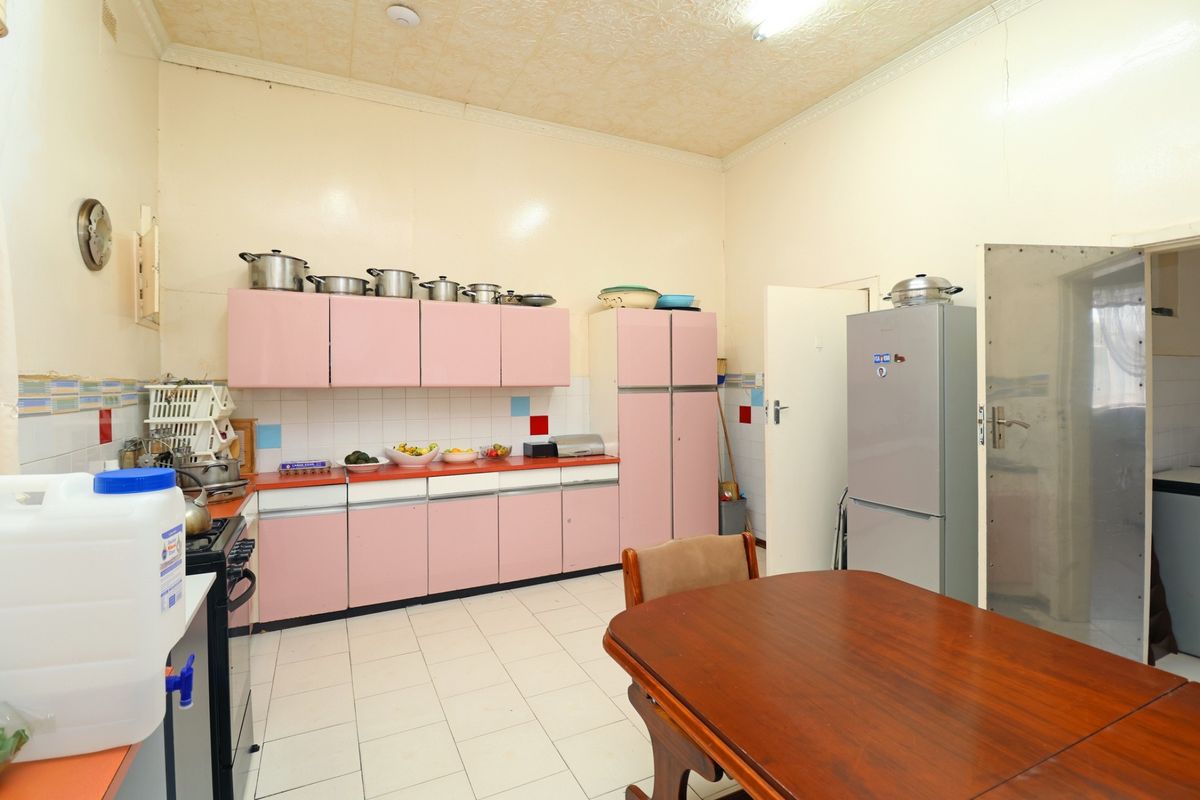 A dated kitchen featuring pink cabinetry, tiled flooring, and a functional layout with built-in storage and workspace.