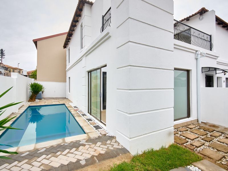 A well-maintained rear exterior featuring a swimming pool, paved patio area, and access to the home via sliding glass doors.