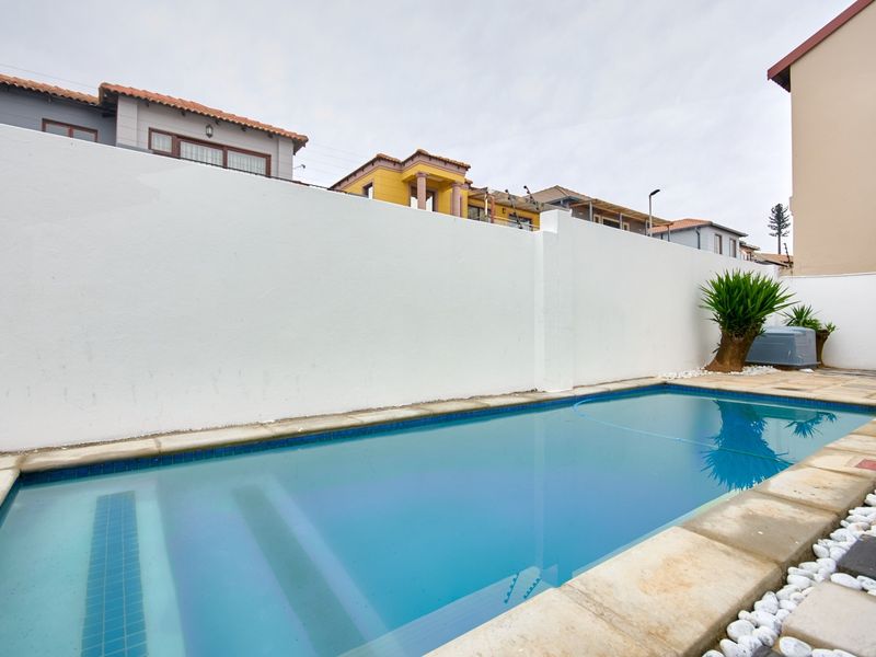 A private swimming pool area featuring a clear blue pool with integrated steps and a high boundary wall for privacy.