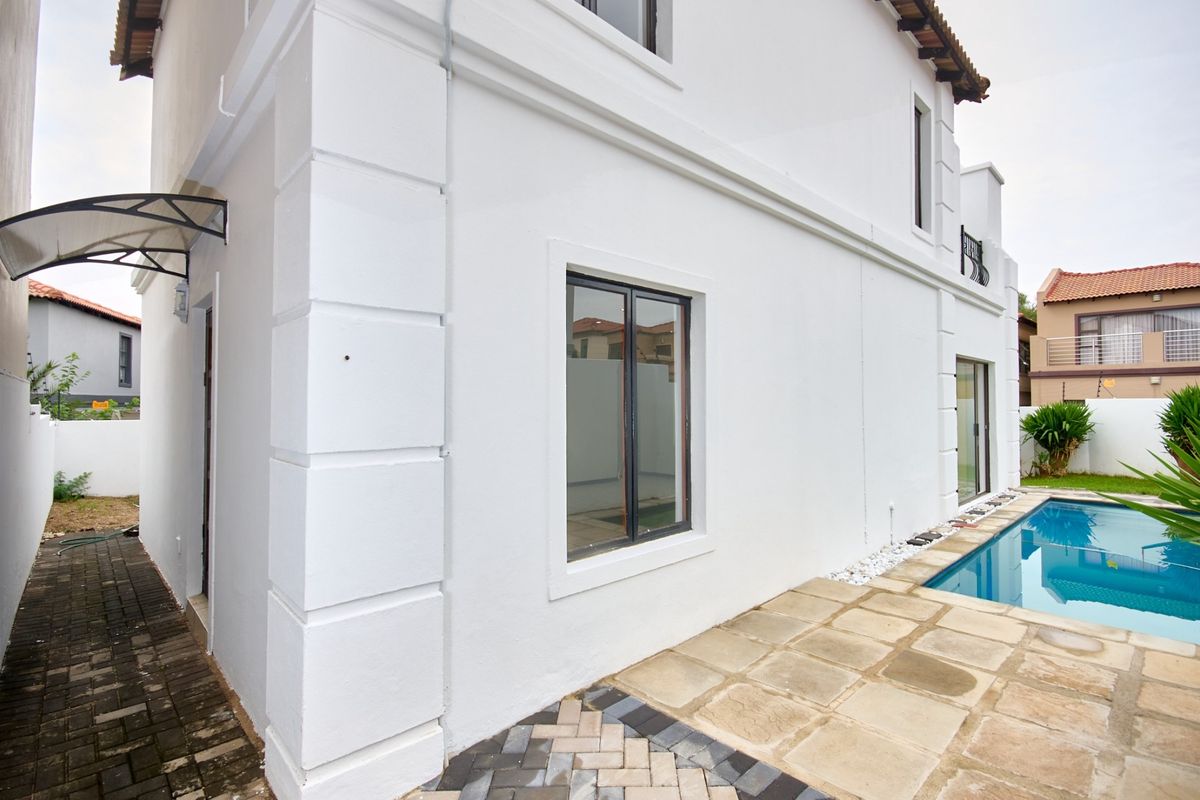 Rear exterior view of the property featuring a swimming pool, paved patio area, and white rendered facade with modern window frames.