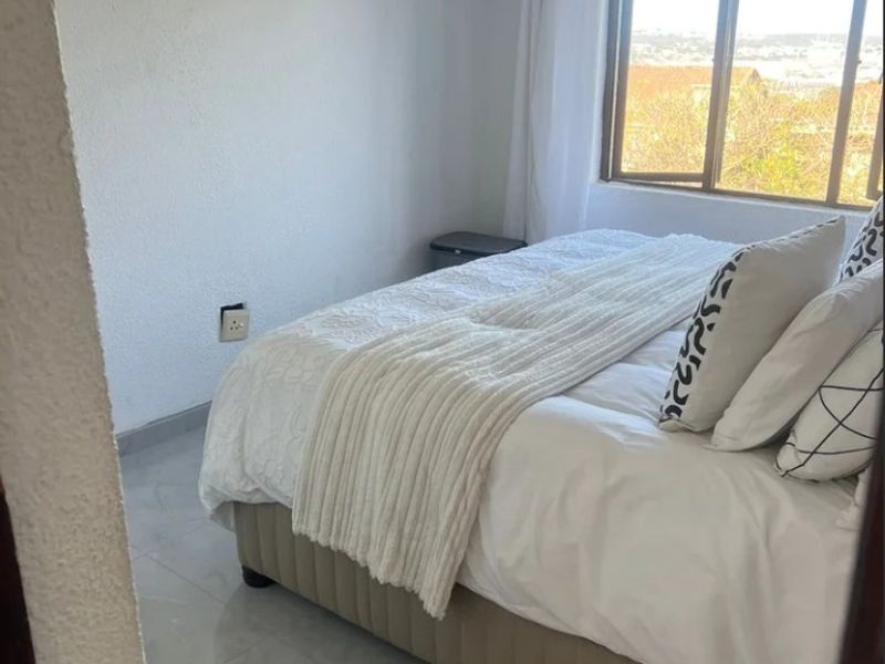 A bright bedroom featuring tiled flooring, a large window with natural light, and neutral wall finishes.