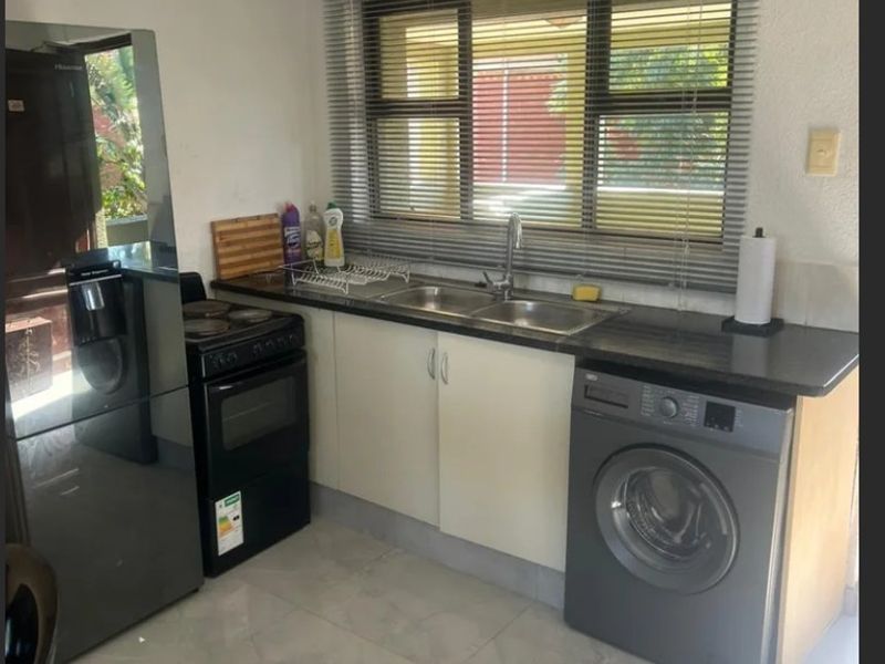 Compact kitchen featuring tiled flooring, laminate countertops, a double sink, and space for a freestanding stove and washing machine.